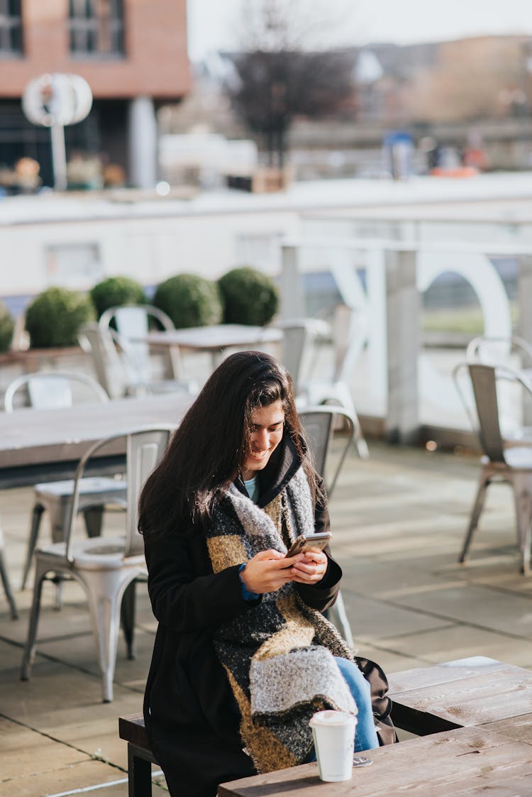 Happy Hispanic Woman Surfing Internet On Smartphone In Urban Cafeteria