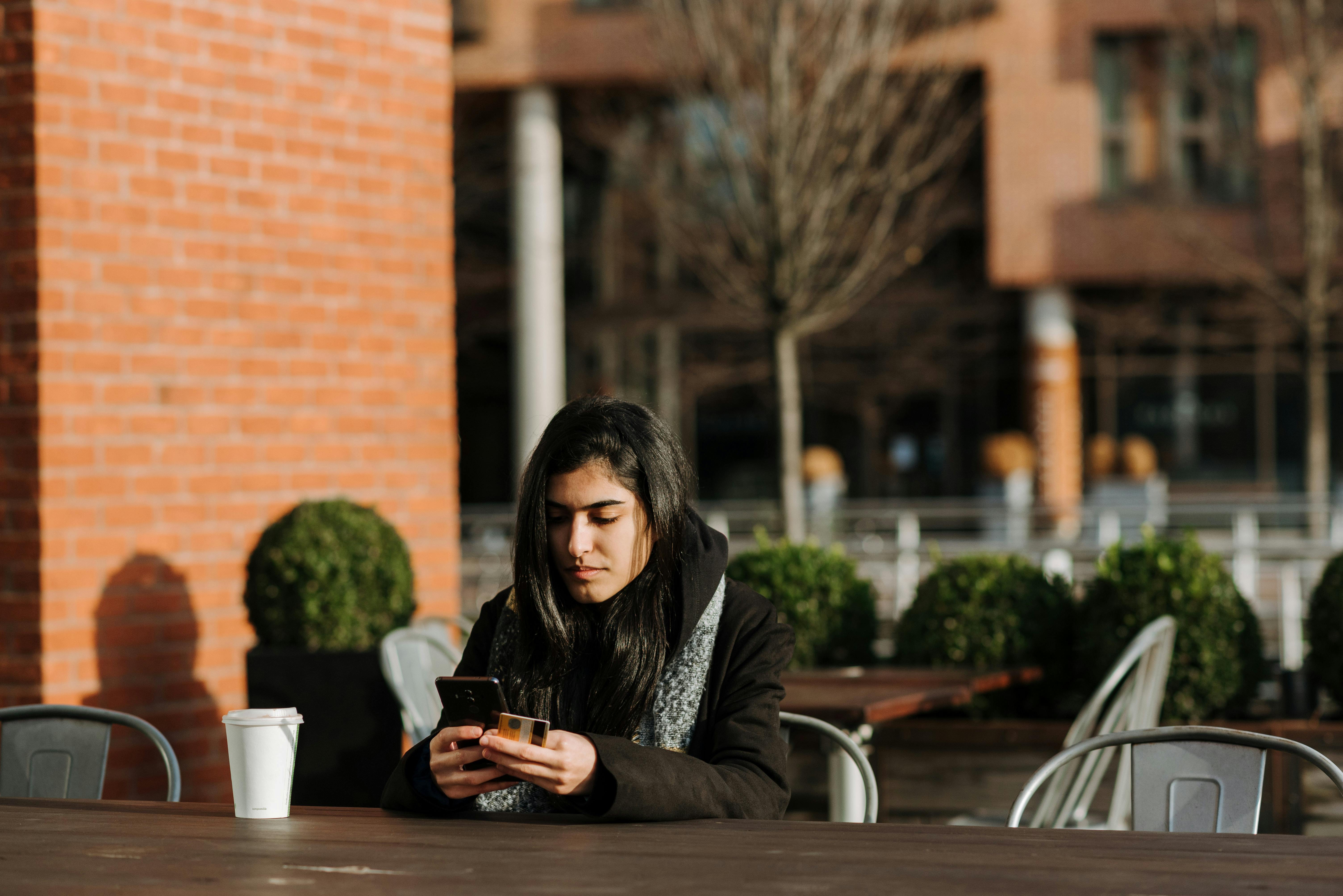 ethnic shopper with smartphone and debit card in street cafe