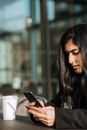 Crop young ethnic female buyer with cellphone and credit card making purchase in street cafeteria with takeaway coffee