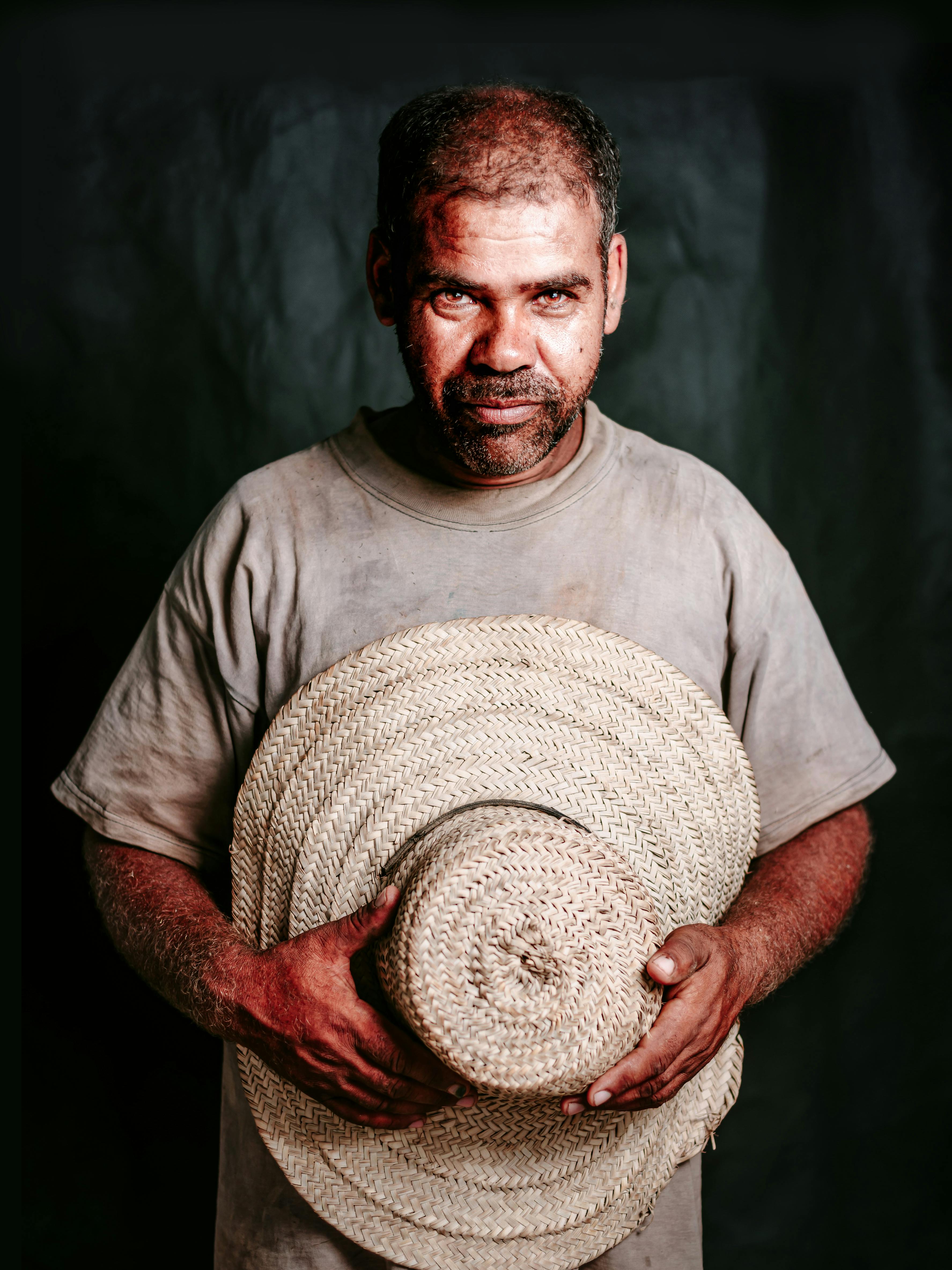 A gritty portrait of a determined farmer holding a sunhat, captured in a studio setting.