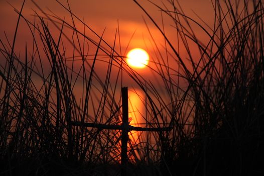 A stunning silhouette of a cross and grass against a glowing sunset sky.