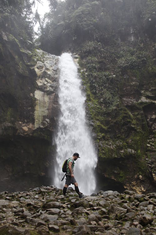 Photo of a Man Walking on Rocks Near a Waterfall