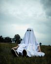 Low angle of child playing ghost in imaginary game and sitting on grass in park