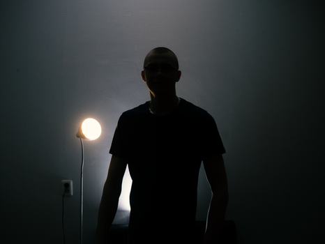 Mysterious silhouette of a man standing in a dark room illuminated by a single lamp.