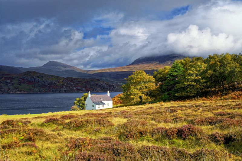 White cottage beside a Scottish loch with Highland mountains in the background