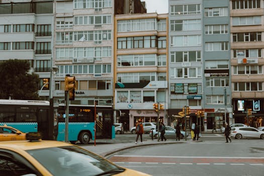 Busy city intersection with buses, taxis, and pedestrians on a cloudy day.