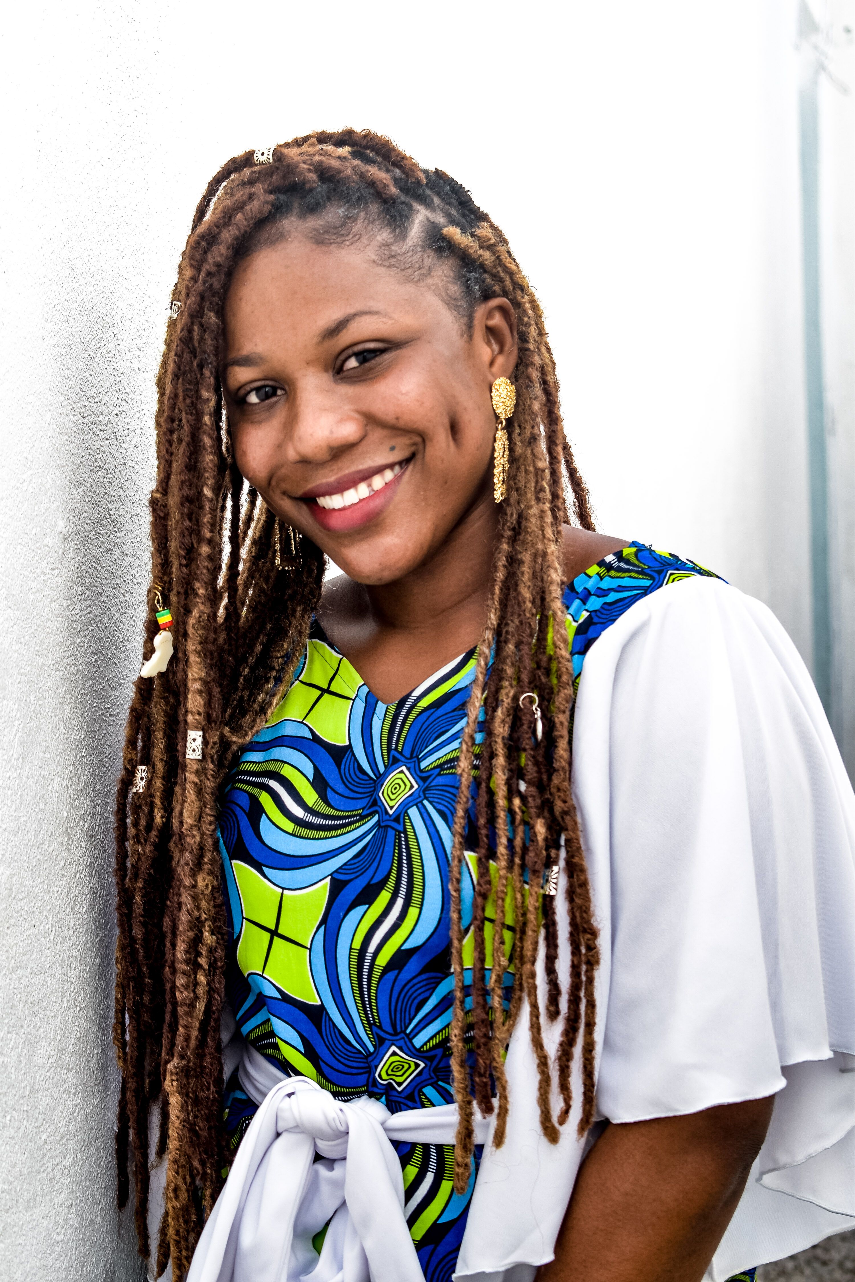 A vibrant portrait of a smiling woman with dreadlocks in colorful attire against a white background.