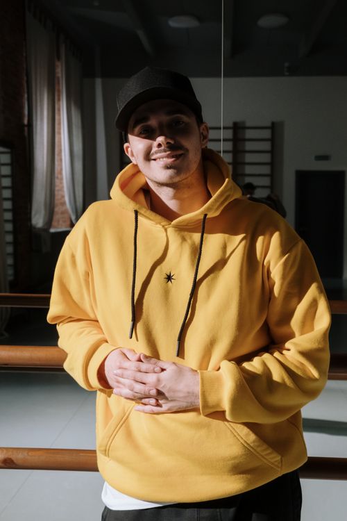 Free Smiling man in a yellow hoodie indoors, standing confidently in a dance studio. Stock Photo