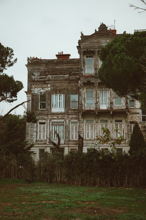 Free A dilapidated mansion with vintage architecture amidst a garden setting, showcasing intricate exterior details. Stock Photo