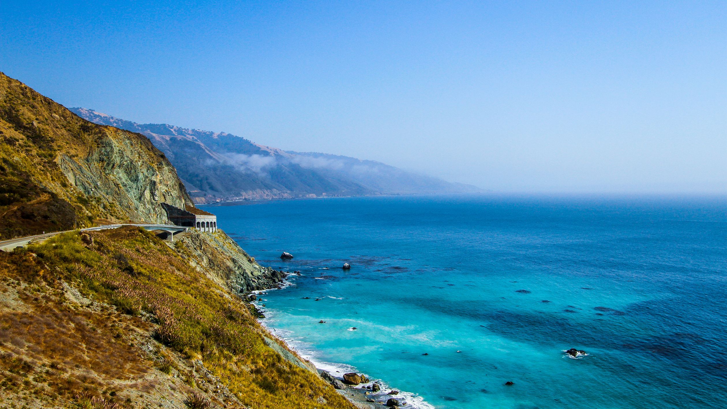 Breathtaking view of the Big Sur coastline with turquoise waters and rugged cliffs under a clear blue sky.