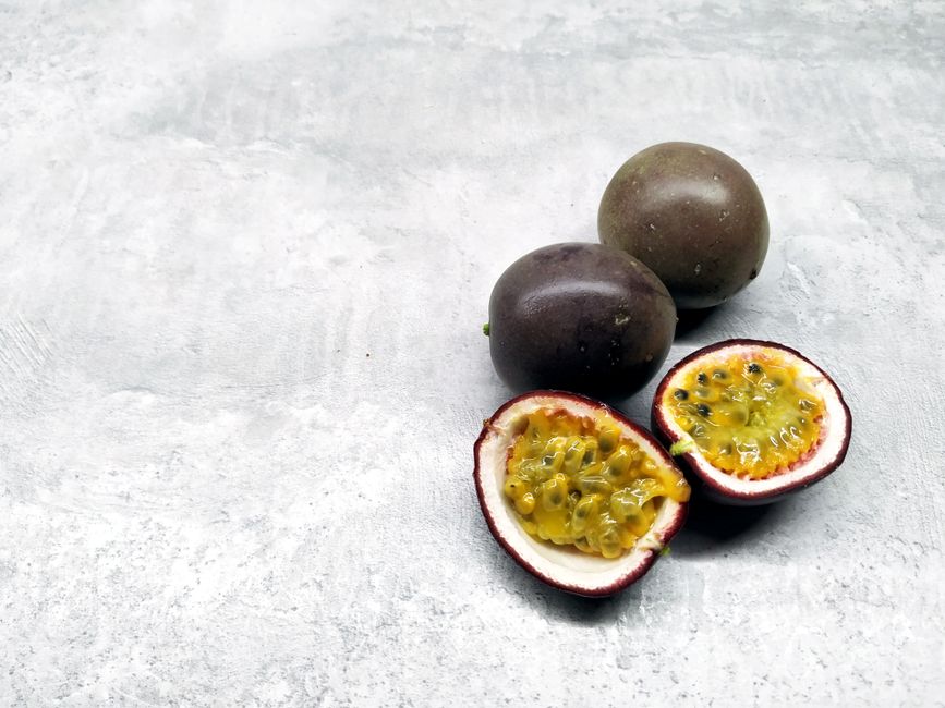 Fresh wrinkled passionfruit halves next to chunks of vibrant frozen mango - thick passionfruit smoothie bowl Fresh wrinkled passionfruit halves next to chunks of vibrant frozen mango - thick passionfruit smoothie bowl