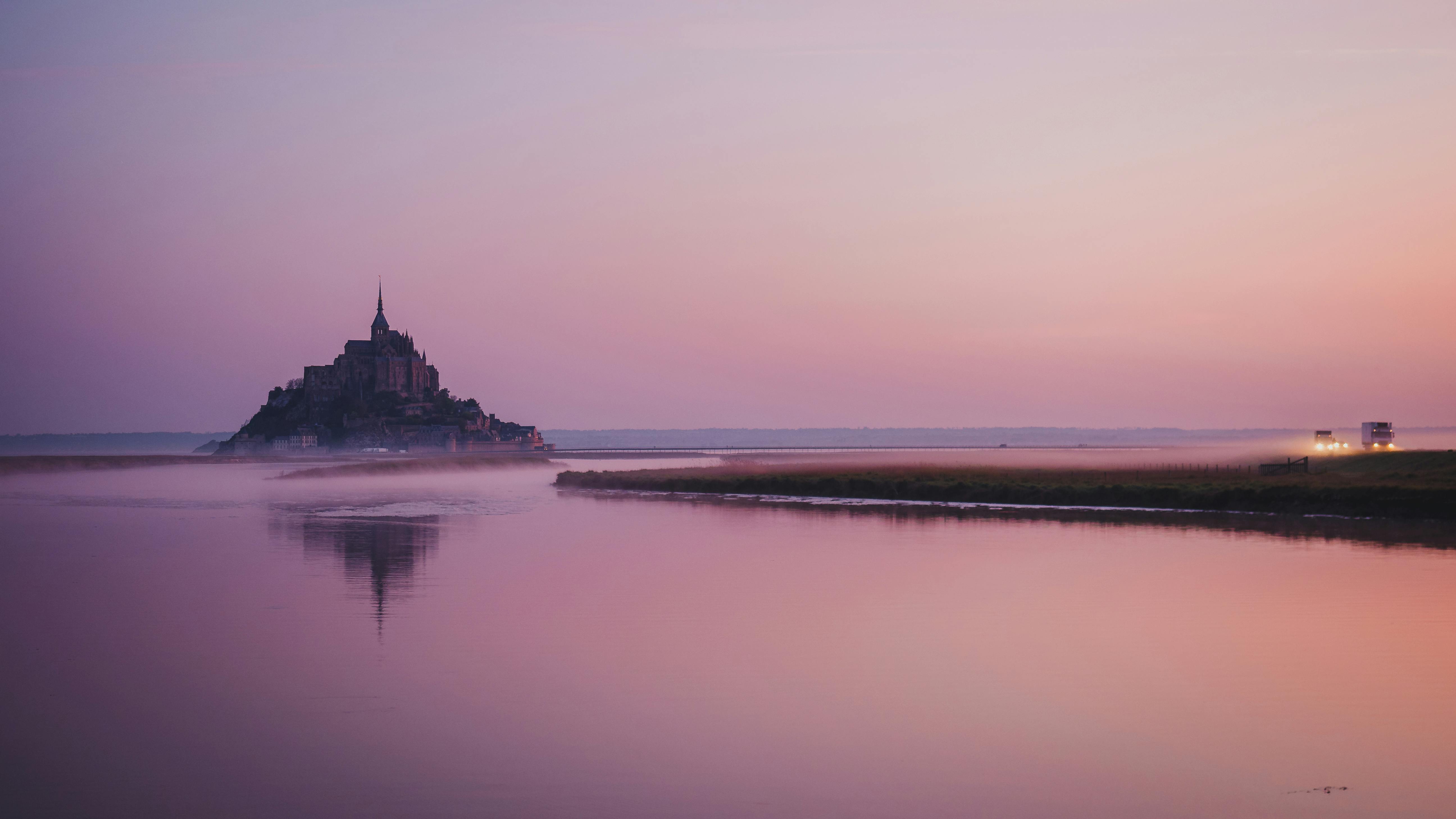 A stunning view of Mont Saint-Michel at dawn with beautiful pink and purple skies reflecting in the water.