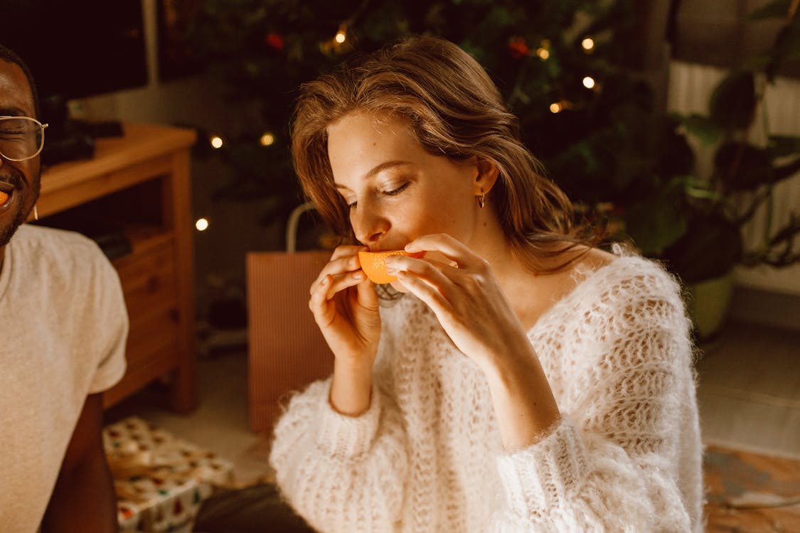 Free A Woman Wearing a Knitted Sweater Eating a Sliced Orange Stock Photo