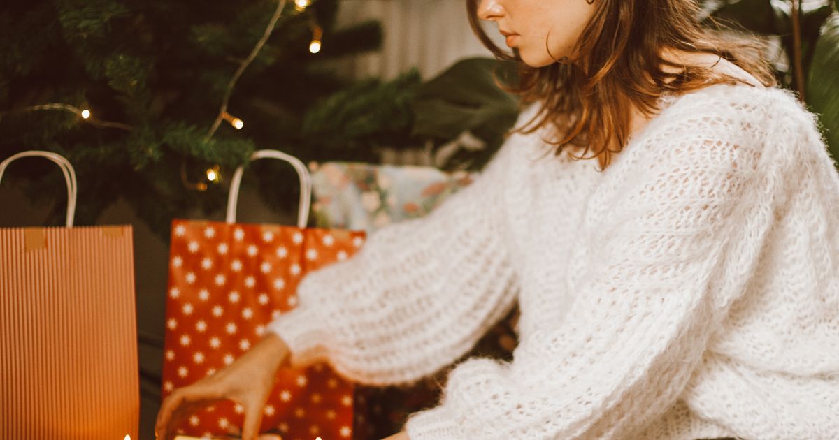 A woman standing with holiday gift bags near a brightly decorated Christmas tree