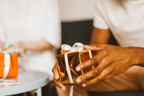 Free A close-up of hands holding a beautifully wrapped golden gift box with a white ribbon, indoors. Stock Photo