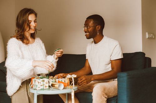Free Two friends enjoying gift wrapping and conversation on a cozy sofa indoors. Stock Photo