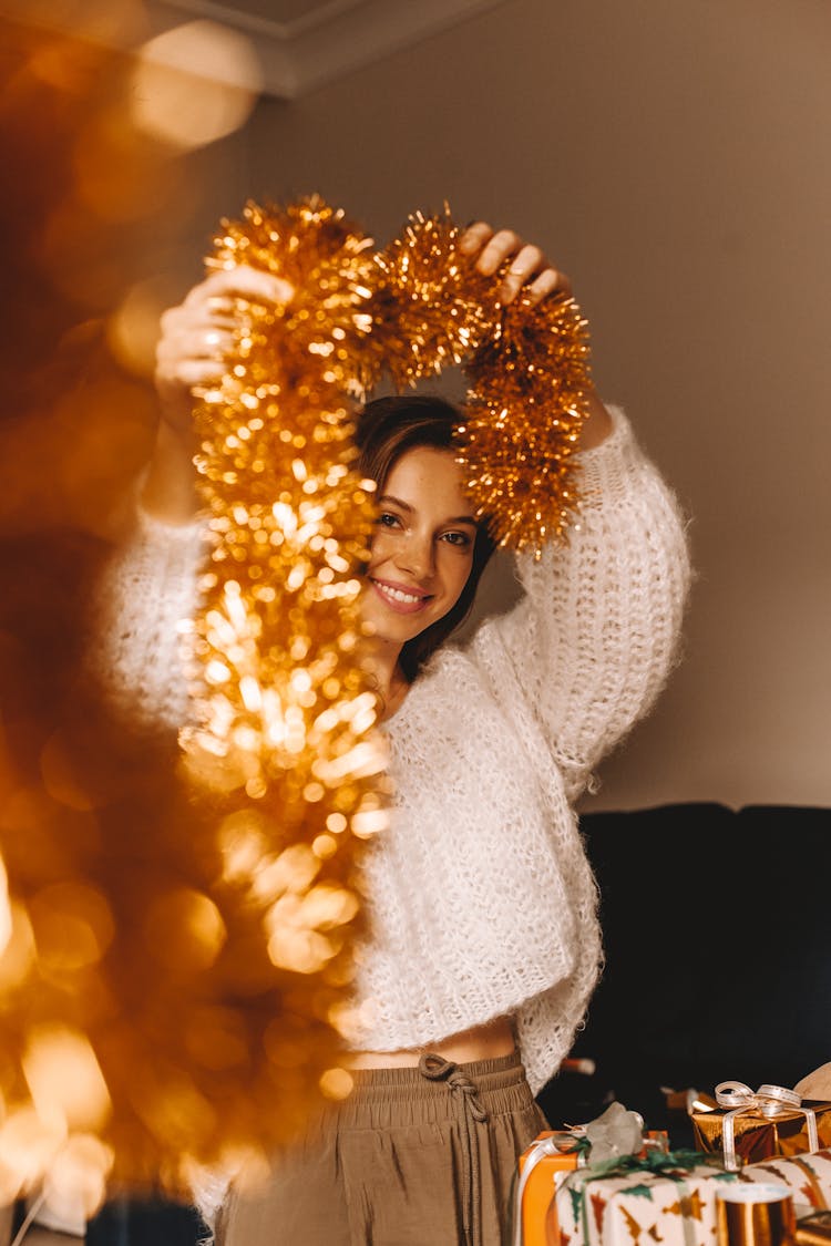 A Woman In White Knitted Sweater Holding A Gold Tinsel