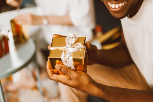 Free Close-up of hands holding a gold gift box with a ribbon, capturing a joyful indoor moment. Stock Photo