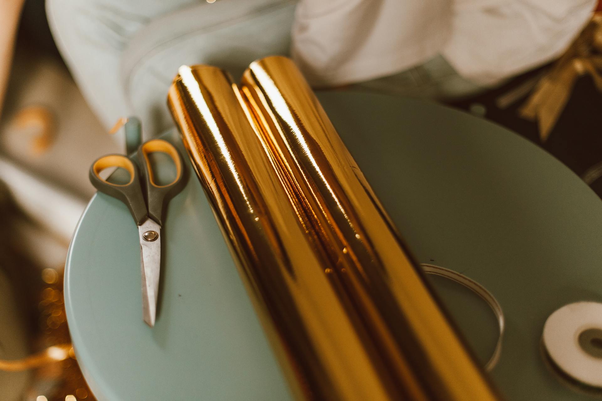 Scissors and golden gift wrap rolls on a table, perfect for crafting or gift wrapping inspiration.