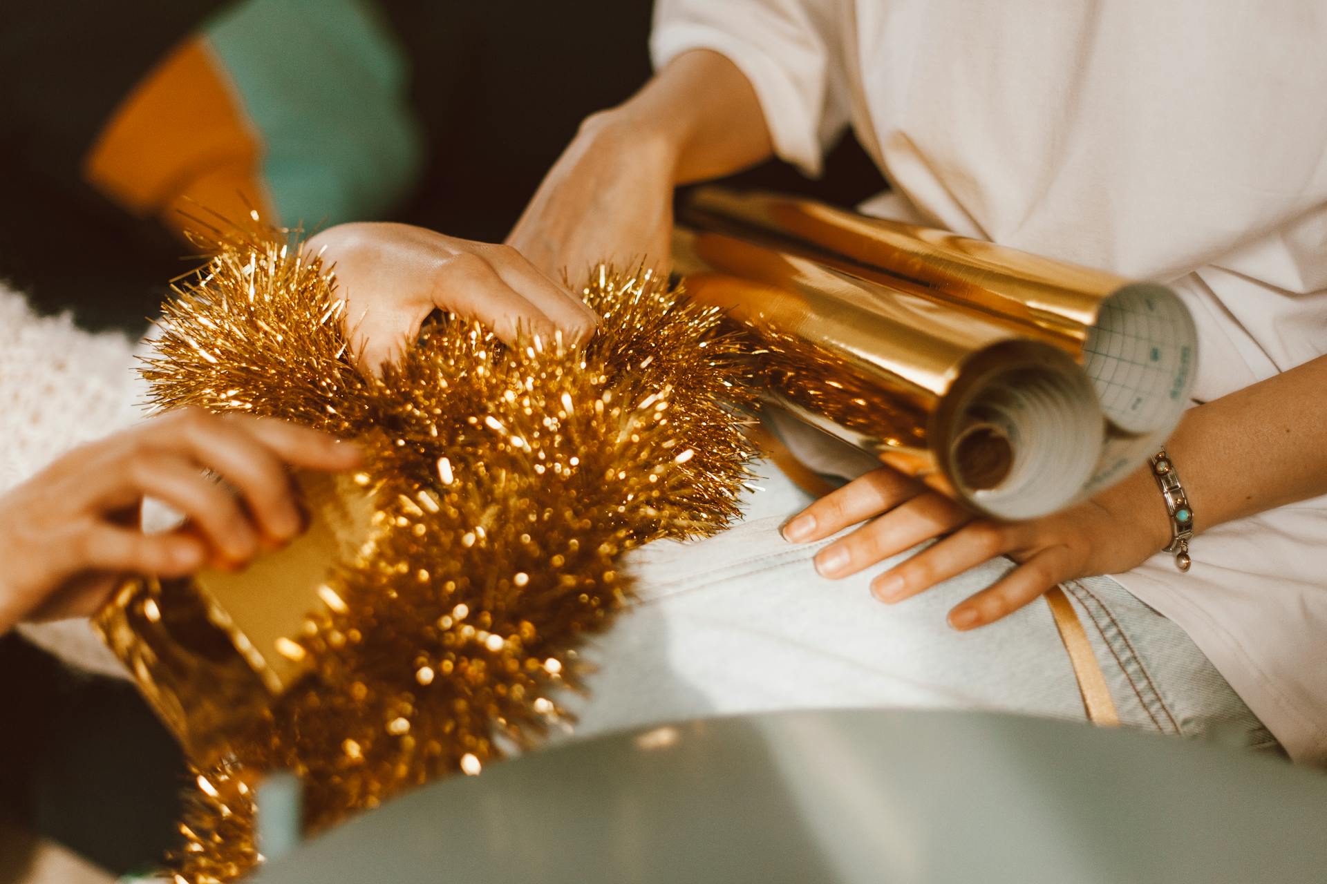 Close-up of hands decorating gifts with gold tinsel and wrapping paper for a festive celebration.