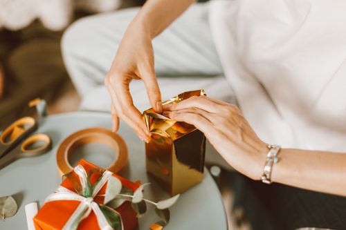 Free Hands wrapping gold and red presents in a cozy indoor setting, perfect for celebrations. Stock Photo