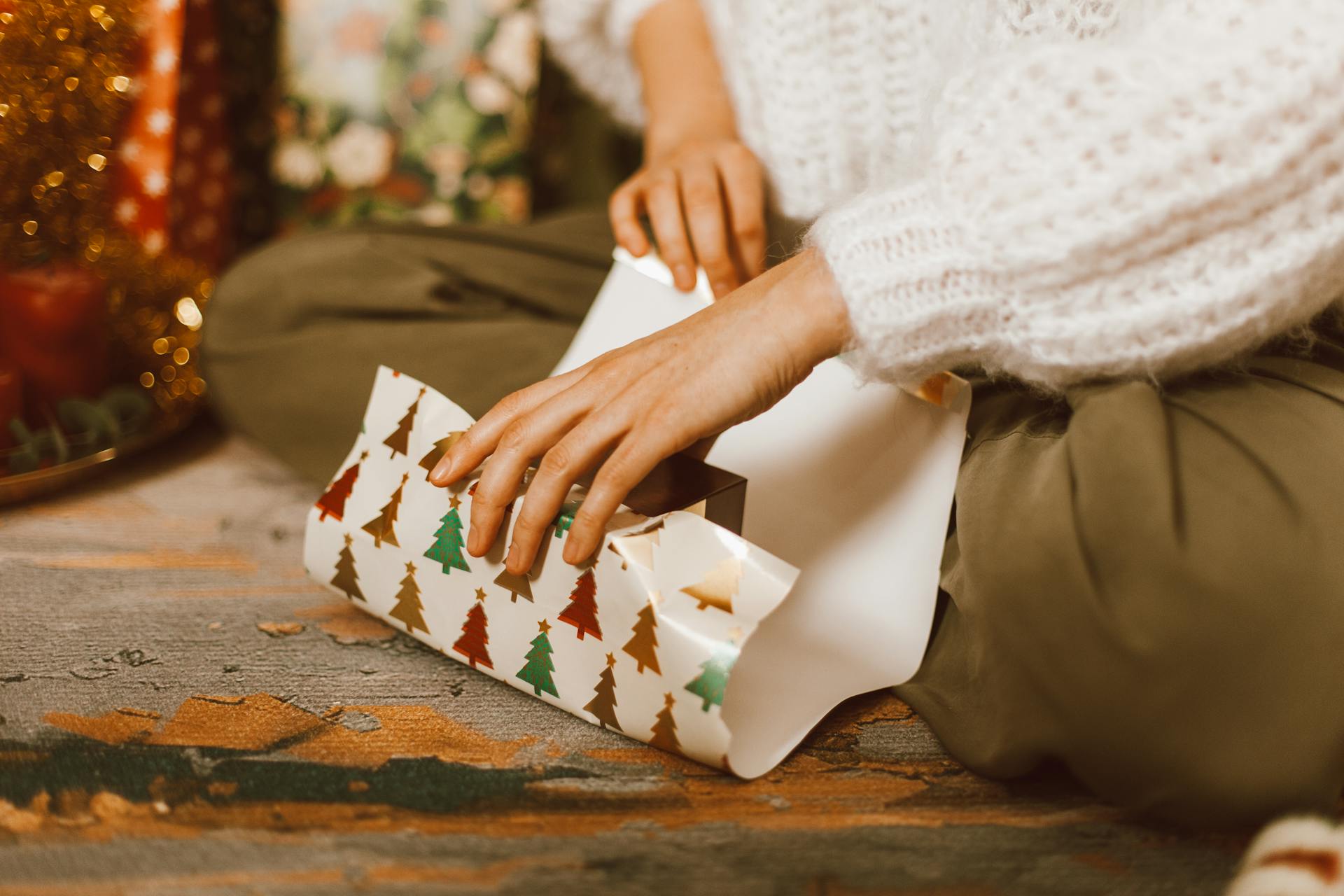 Close-up of a woman wrapping a Christmas gift with festive paper on the floor.