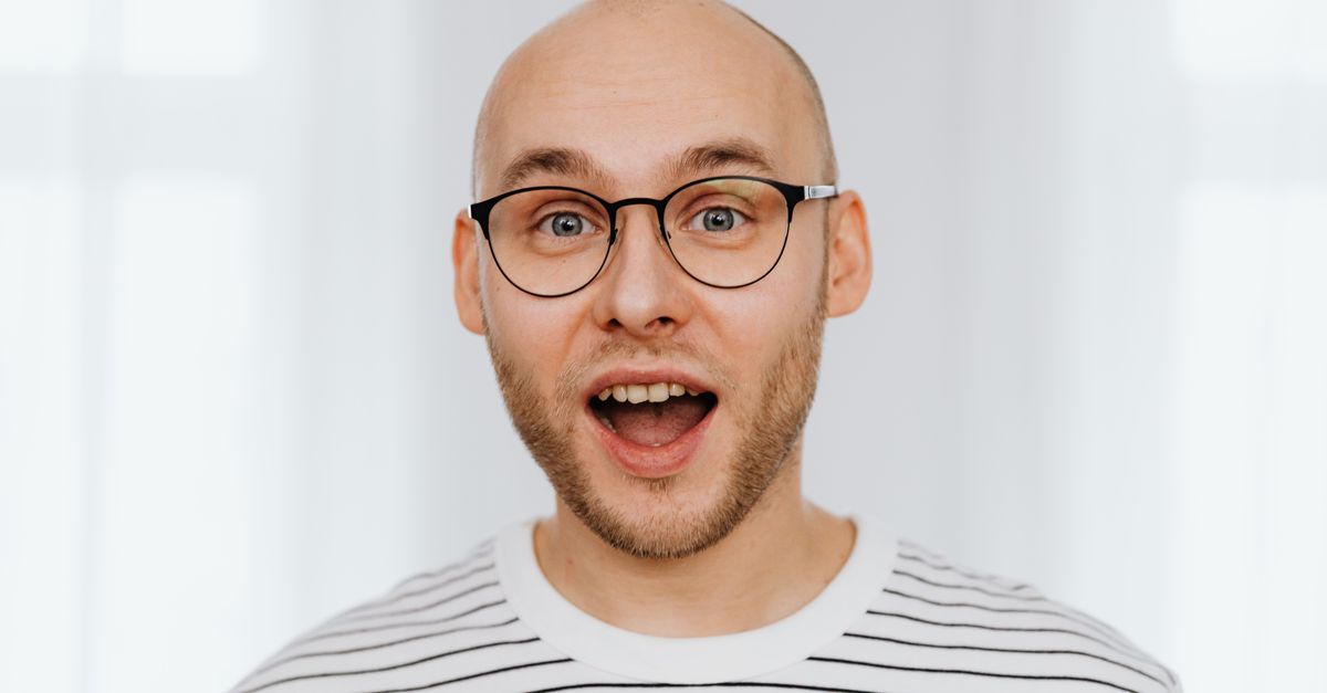 A man in glasses and a striped shirt, at ease with a shaved head.
