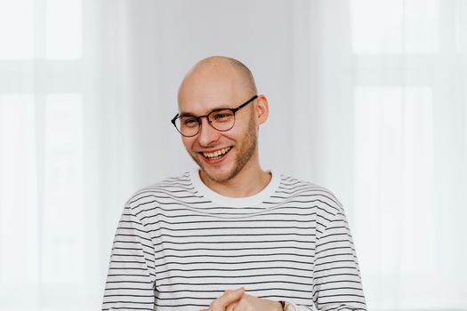 A bald man with glasses and a joyful smile in a striped shirt indoors.