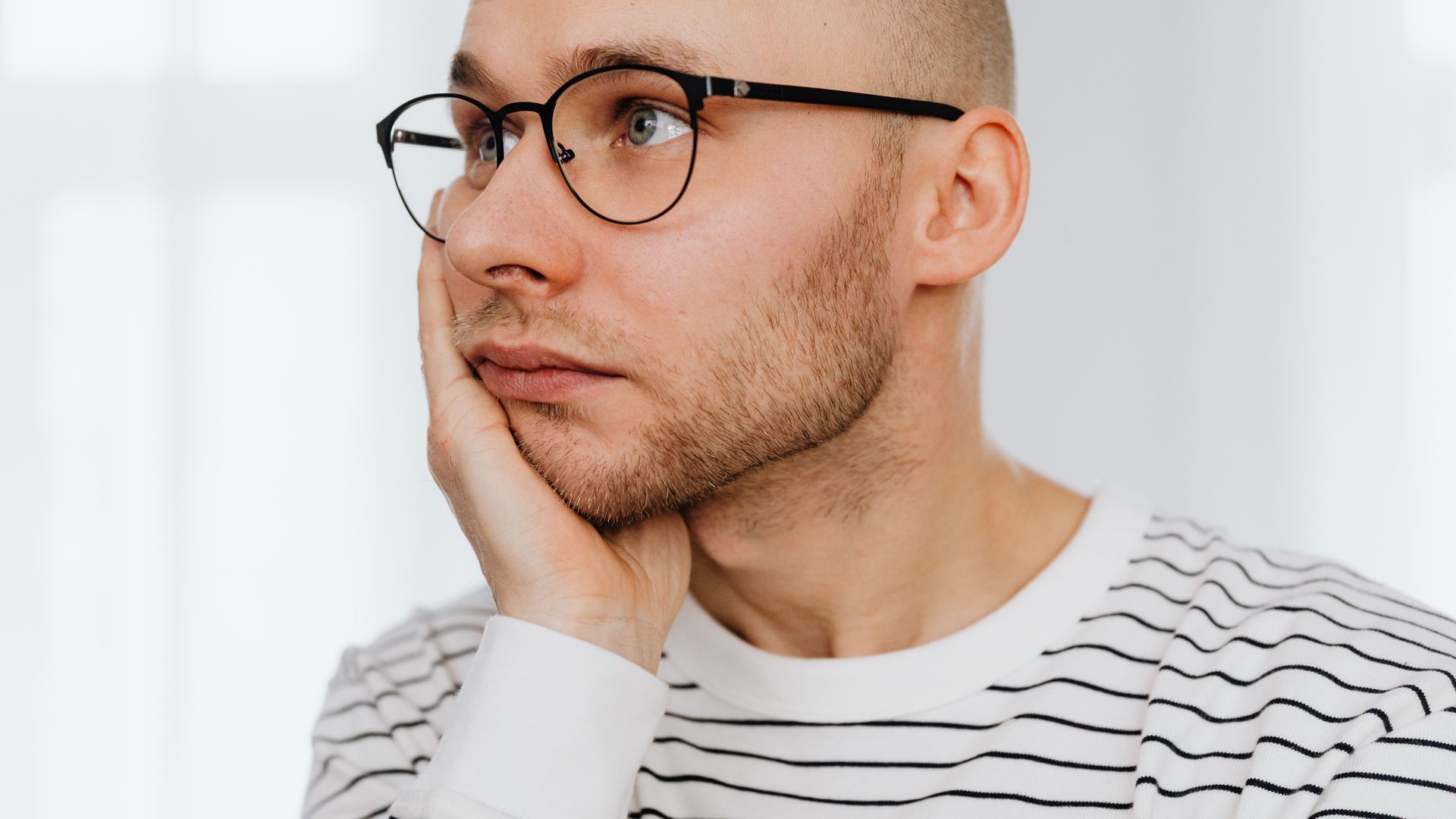 Modafinil Hair Thinning Myth: Unraveling the Truth Close-up portrait of a young man with glasses, looking pensive indoors — modafinil hair thinning myth
