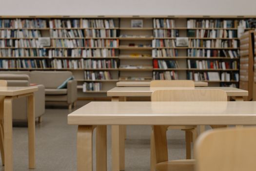 A modern library interior featuring wooden tables, chairs, and bookshelves filled with books.