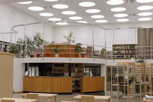Free Spacious library interior with bookshelves, desks, and unique circular ceiling lights. Stock Photo