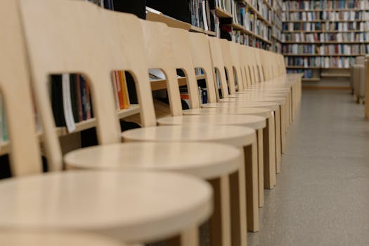 Row of wooden chairs in a university library with bookshelves in the background, ideal for study ambiance.