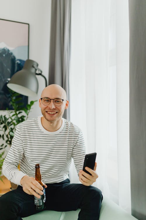 Free A Bald Man Holding a Beer and Smartphone Stock Photo