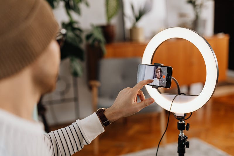Seorang content creator merekam video menggunakan smartphone dan ring light di rumah