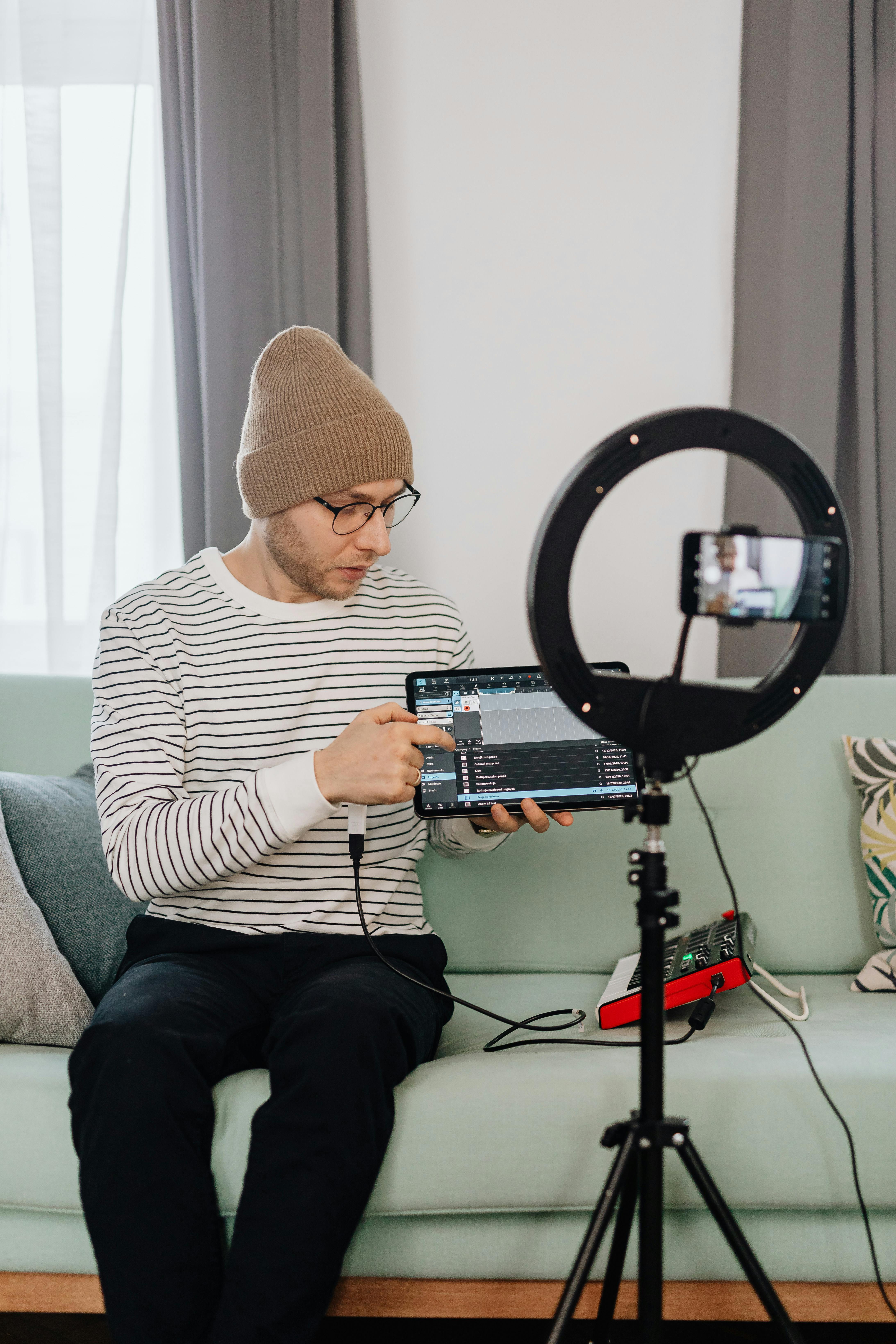 A young man in a striped shirt recording video content with a ring light and tablet.