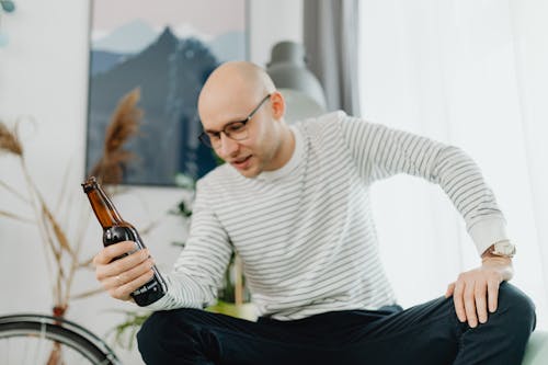Free A Man in Black Pants Sitting while Holding a Glass Bottle Stock Photo