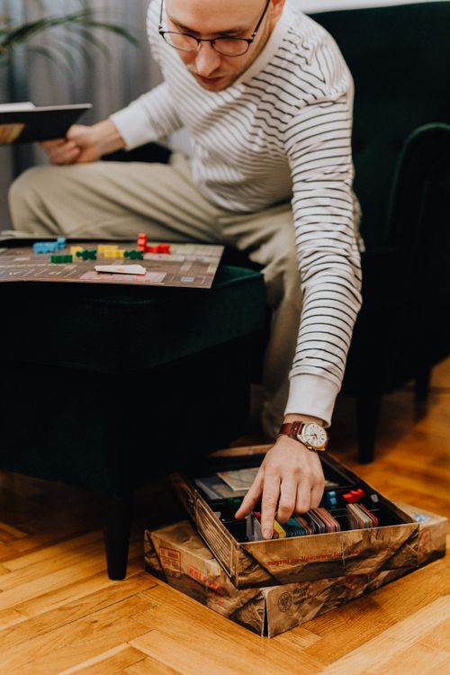 Free A man with glasses and a striped shirt concentrates on a board game in a cozy living room setting. Stock Photo