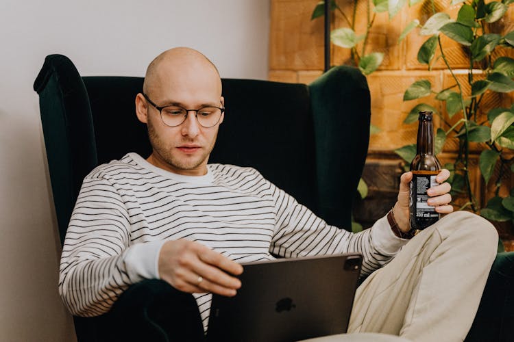 A Man Sitting On An Armchair While Looking At His Ipad