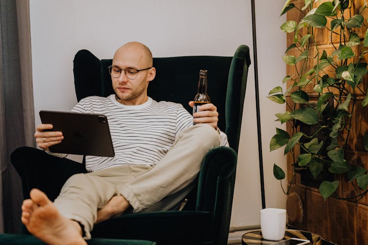 Man Relaxing In Chair With Tablet Drinking Beer