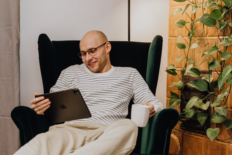 Man Relaxing In Armchair With Tablet And Coffee