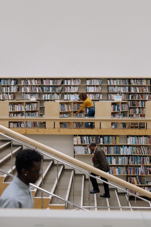 Free Individuals exploring books in a spacious and modern public library setting. Stock Photo