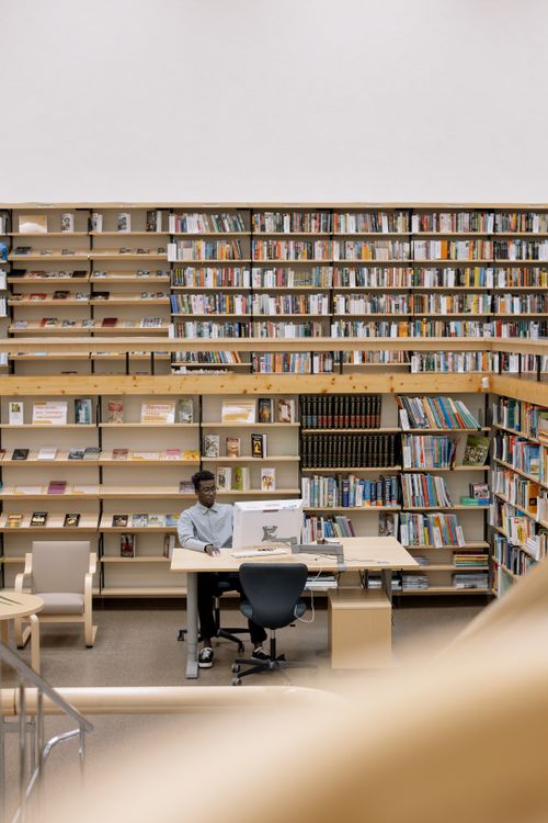 Free A person studying at a desk in a well-lit library with organized bookshelves. Stock Photo