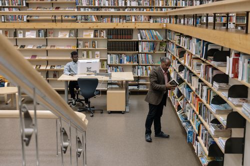Free Interior of a modern library with people reading and browsing books on shelves. Stock Photo