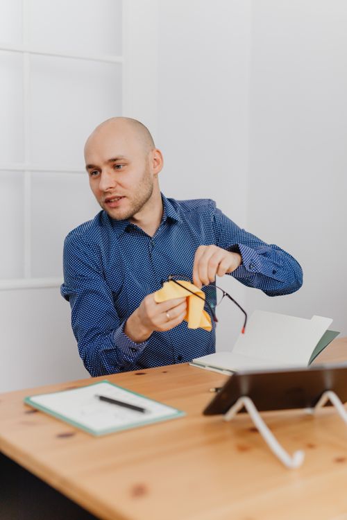 Free Bald man sitting at a desk cleaning a tablet with a cloth in an office setting. Stock Photo