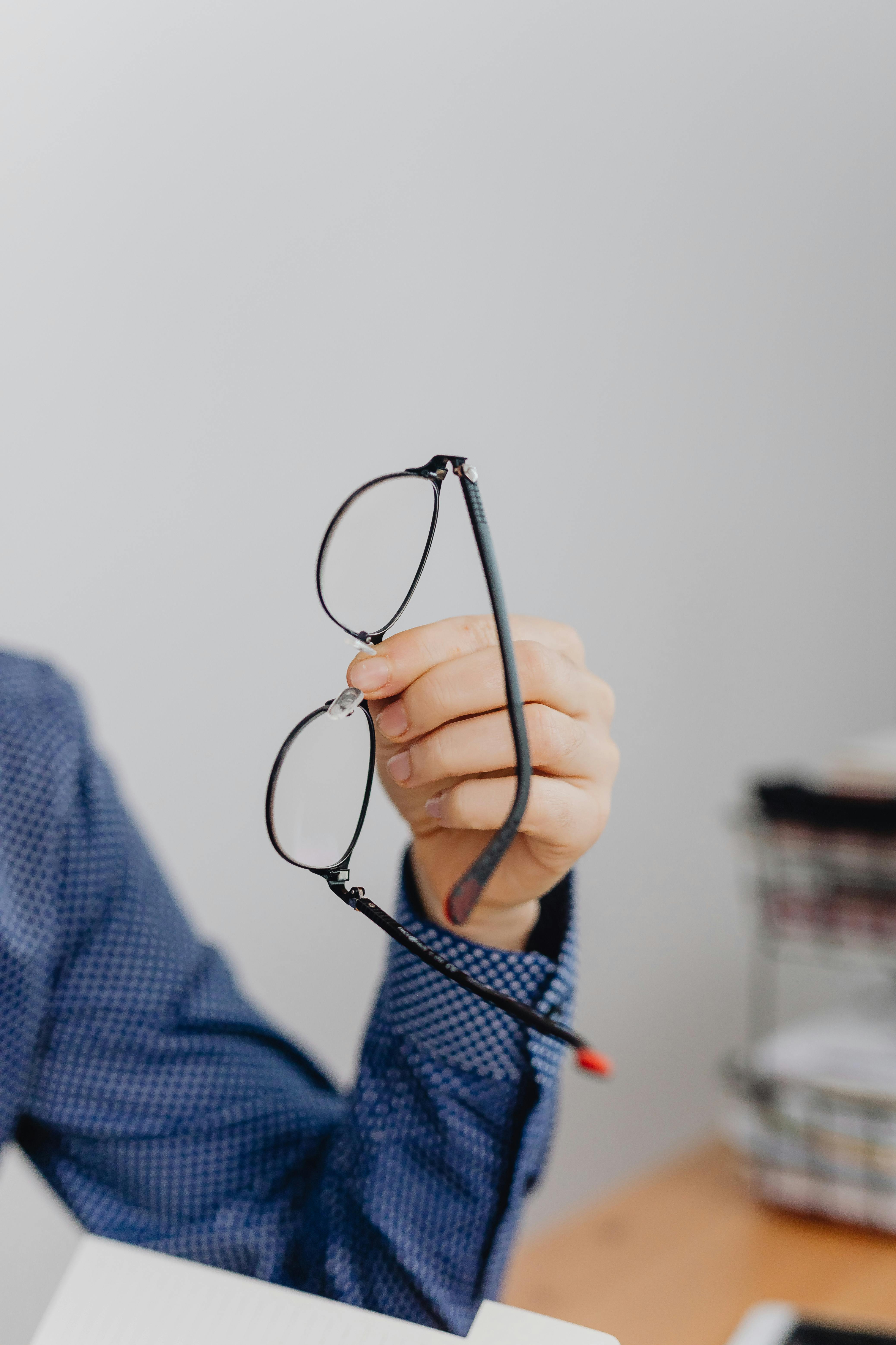 Close-up of a person holding eyeglasses indoors, perfect for office or vision themes.