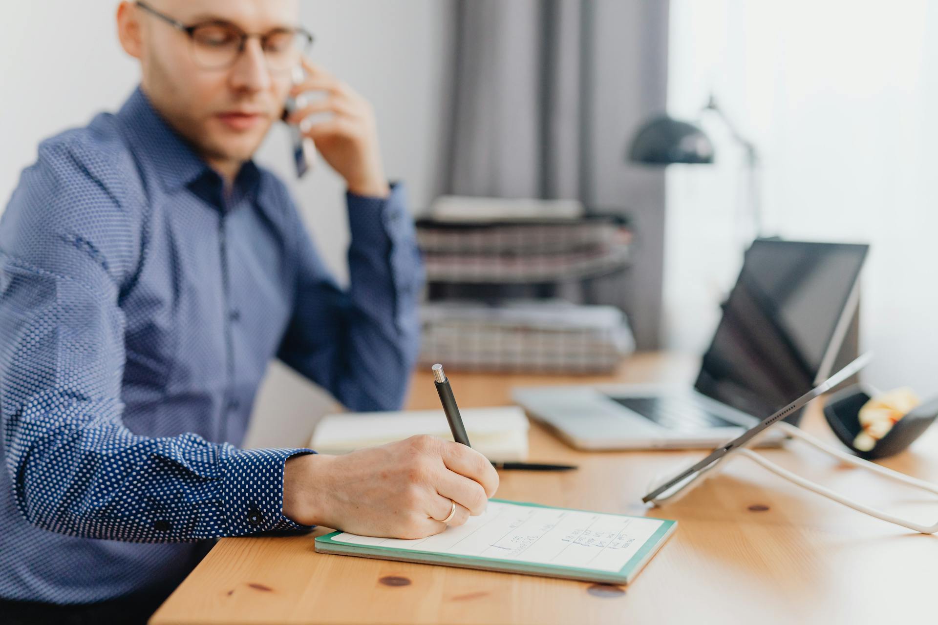 Businessman at a desk with laptop and notebook, focused on work calls and writing notes.