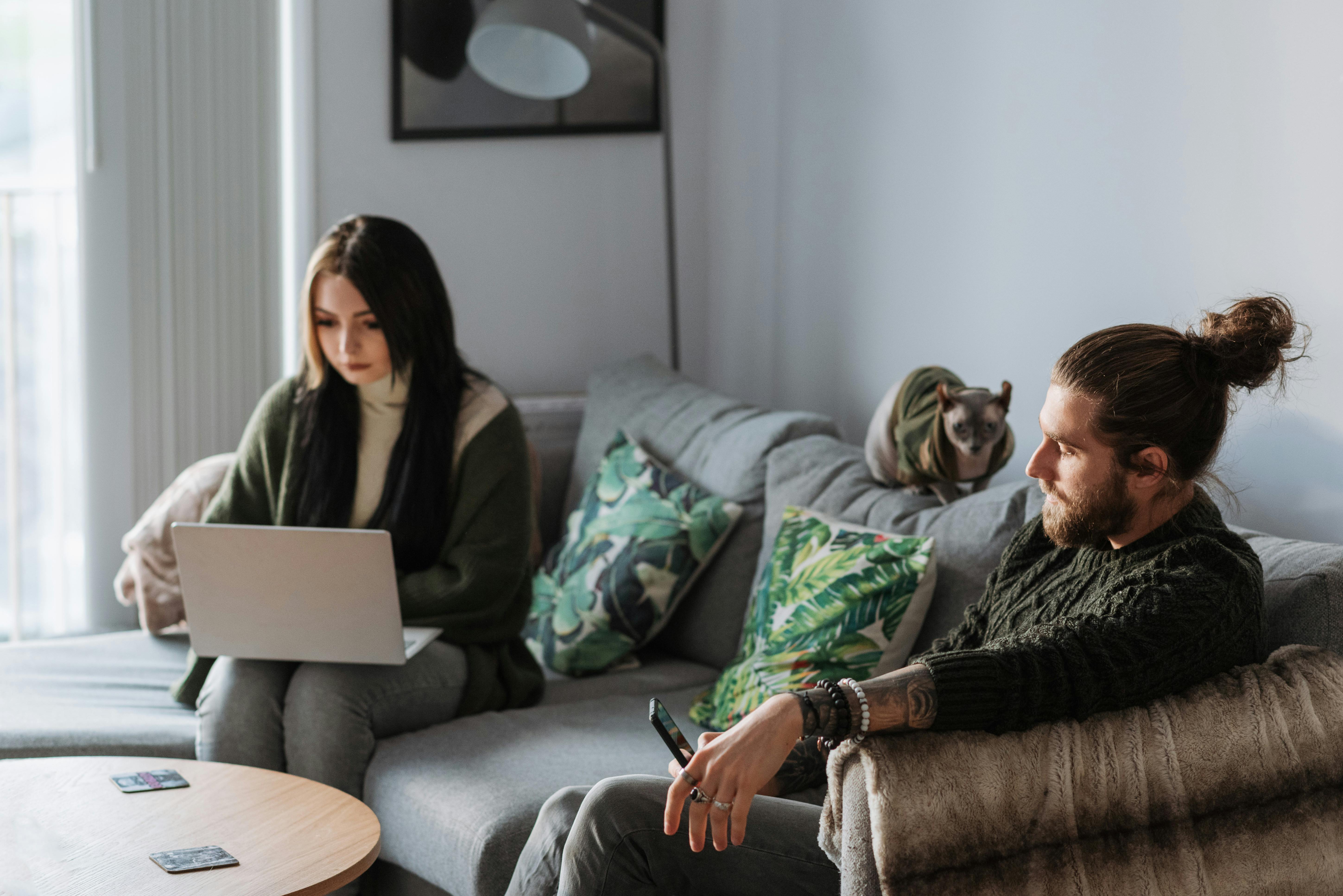 man with smartphone near girlfriend with laptop and cat indoors