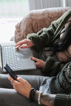 From above side view of crop anonymous couple surfing internet on netbook and cellphone on couch in living room