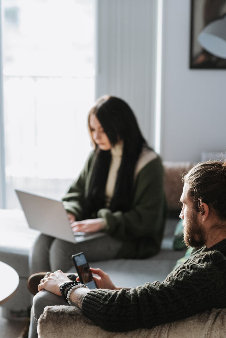 Crop Man Surfing Internet On Smartphone Near Girlfriend With Laptop