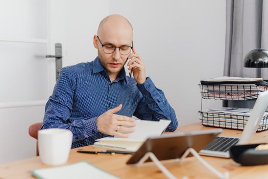 A bald professional man using a phone and making notes in an office environment.